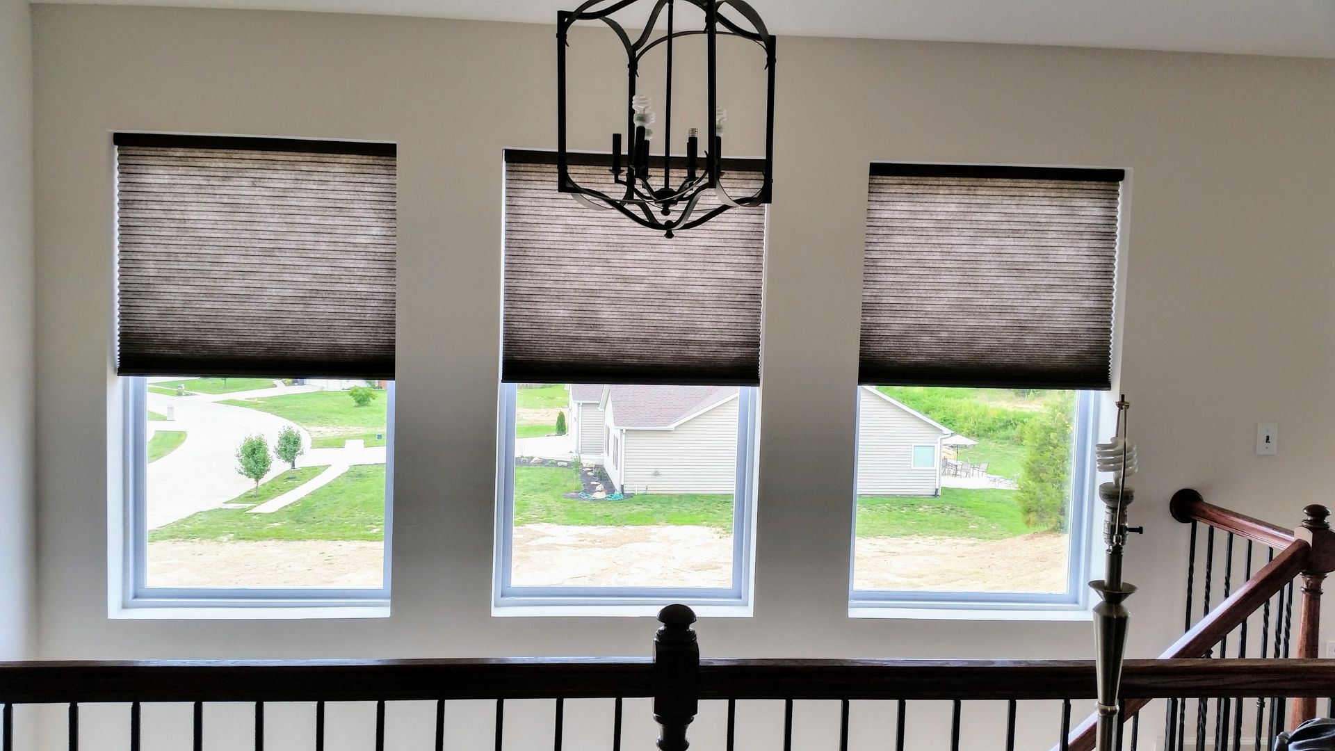 Three windows with dark shades and a black chandelier above. A staircase is on the right.