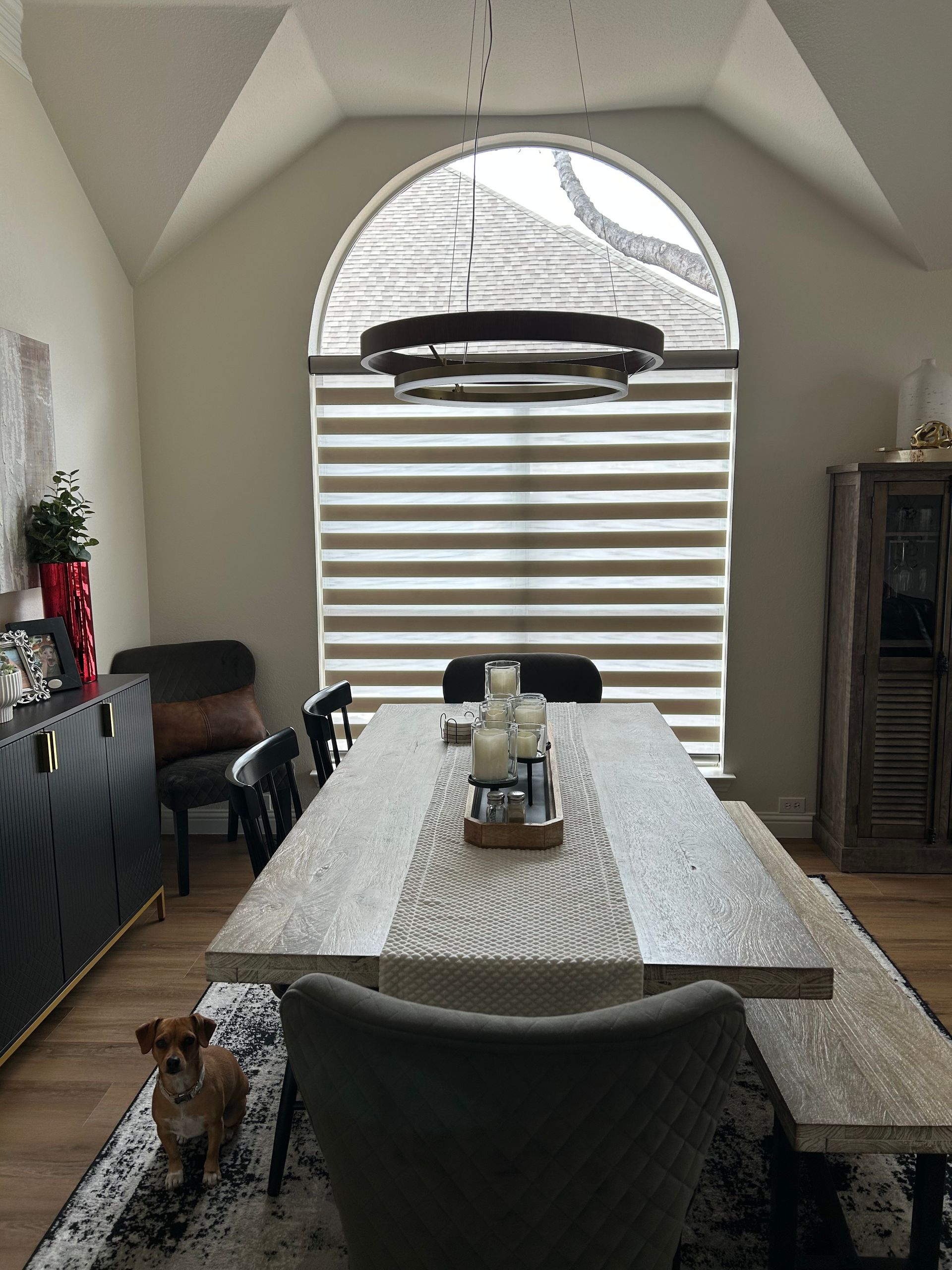 Dining room with arched window, table, chairs, dog, and buffet.