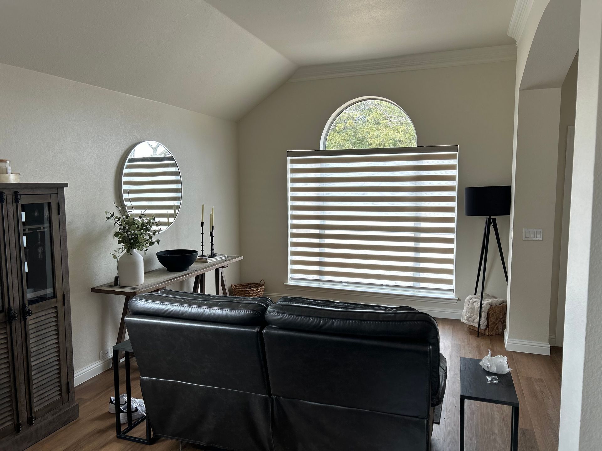 Living room with leather recliner, console table, arched window with striped blinds.