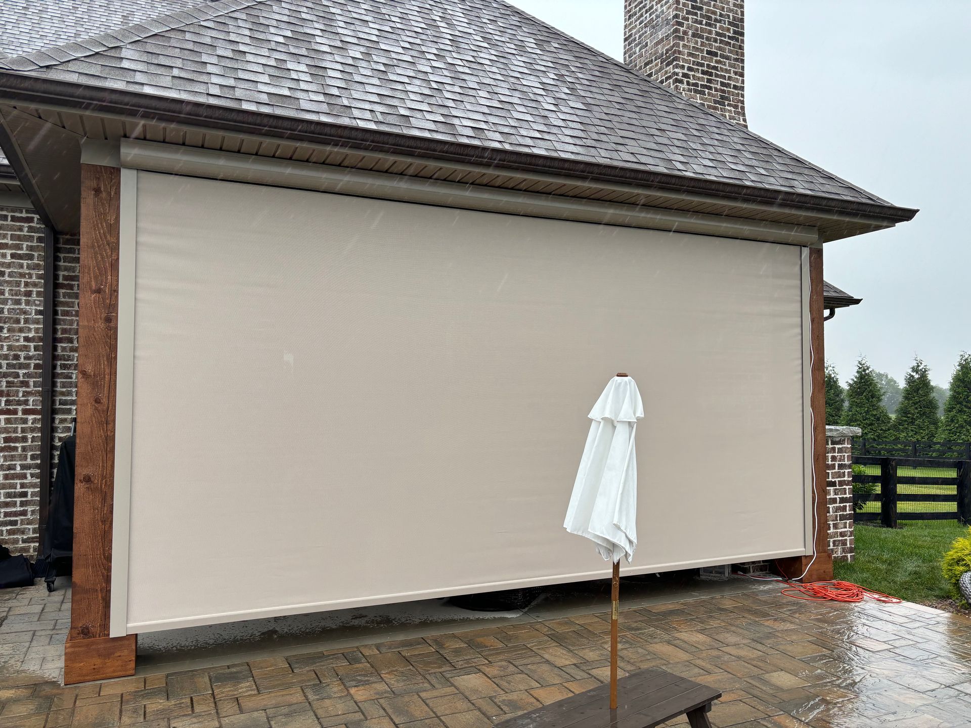 Beige outdoor roller shade on a covered patio, partially obscuring an umbrella.