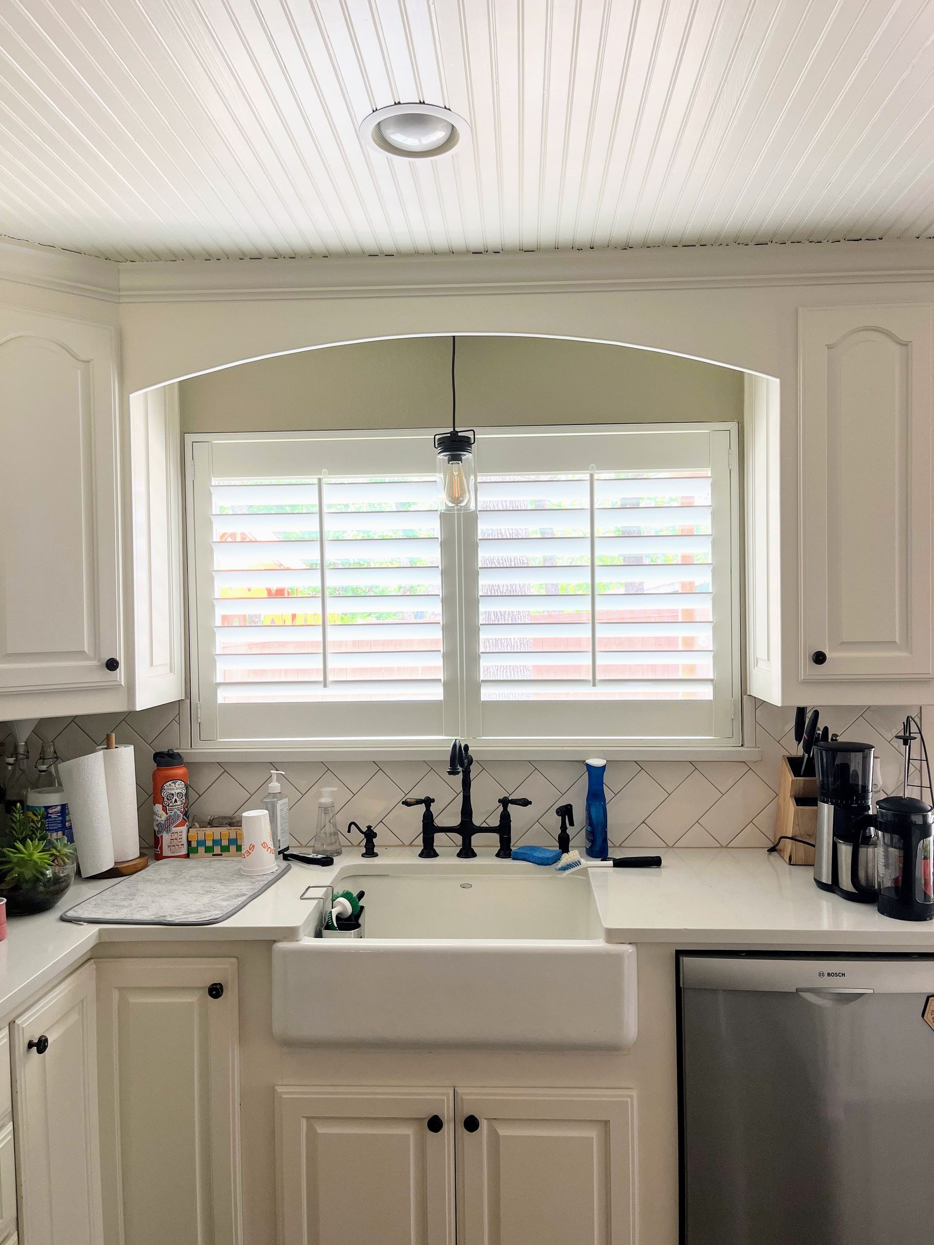 Kitchen with white cabinets, farmhouse sink, window with shutters, and black faucet.