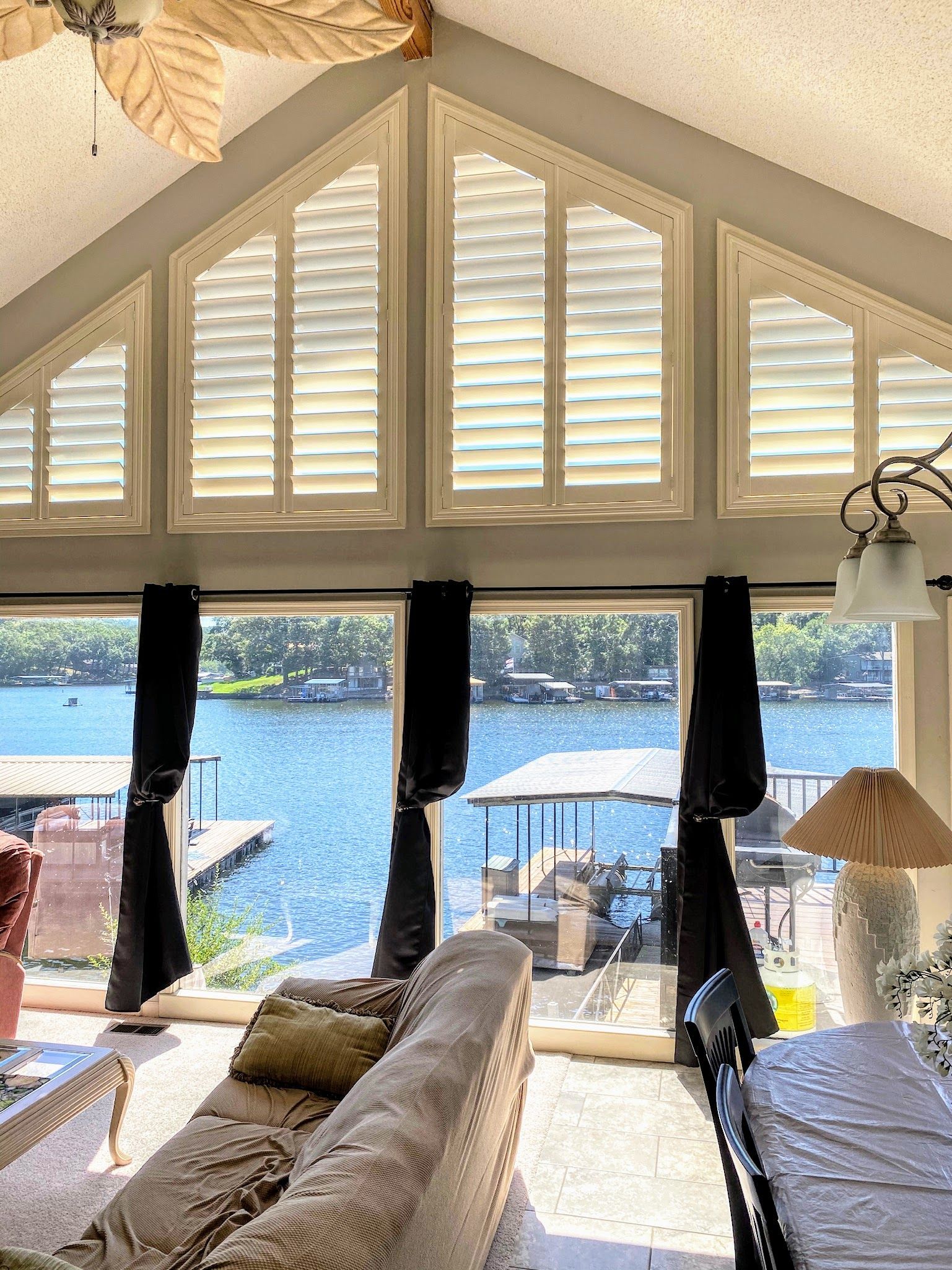 Lake view from a living room with dark curtains, shutters, and a beige sofa.