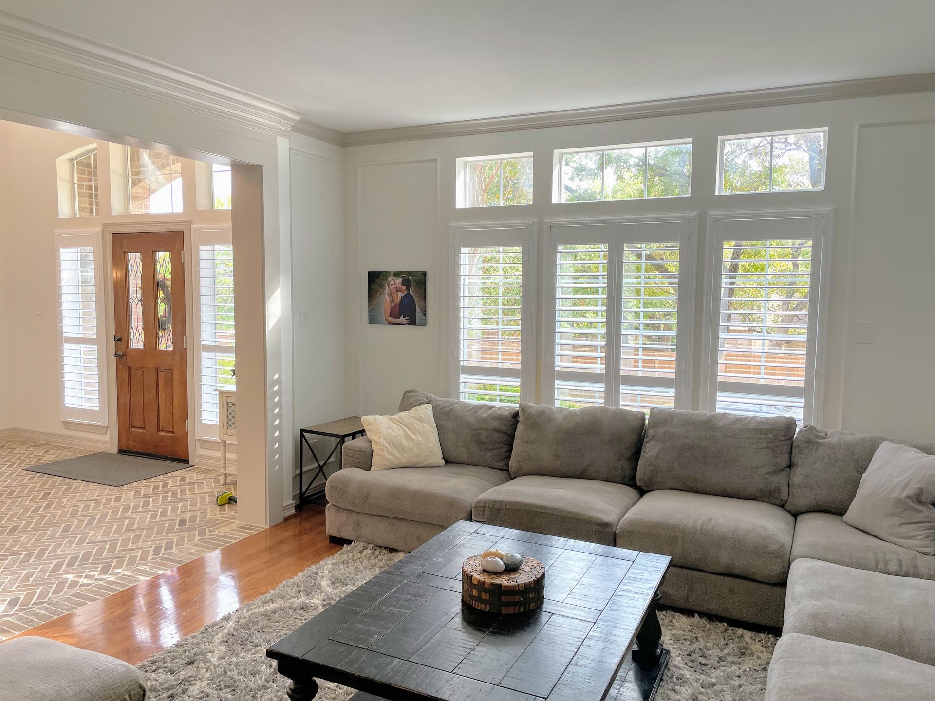 Living room with sectional sofa, window with shutters, and wooden front door.