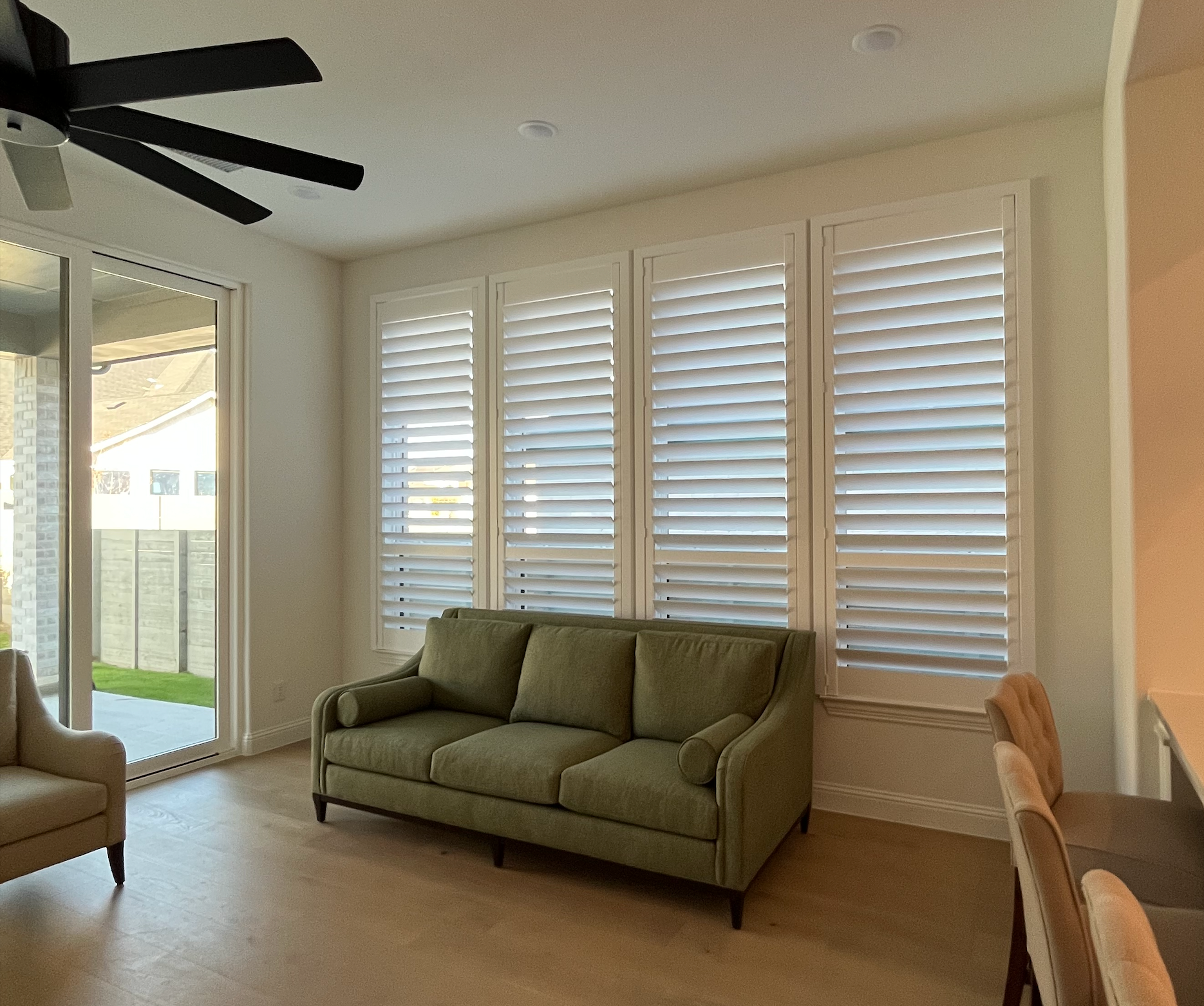Living room with green sofa, white shutters, and a sliding glass door.