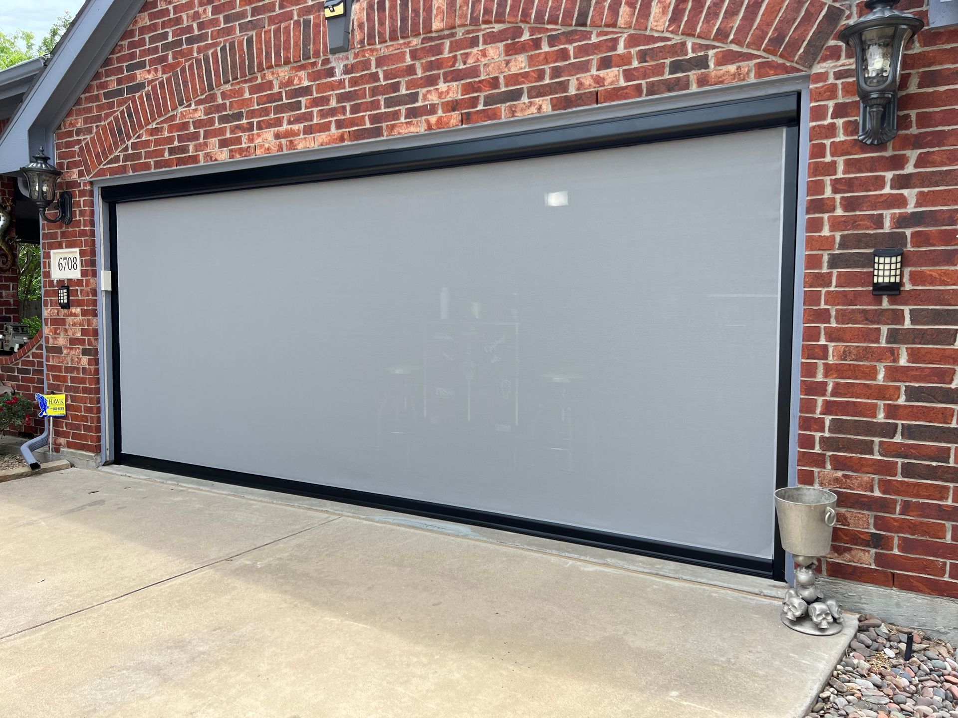 Garage door with grey screen lowered against a red brick building, black frame.