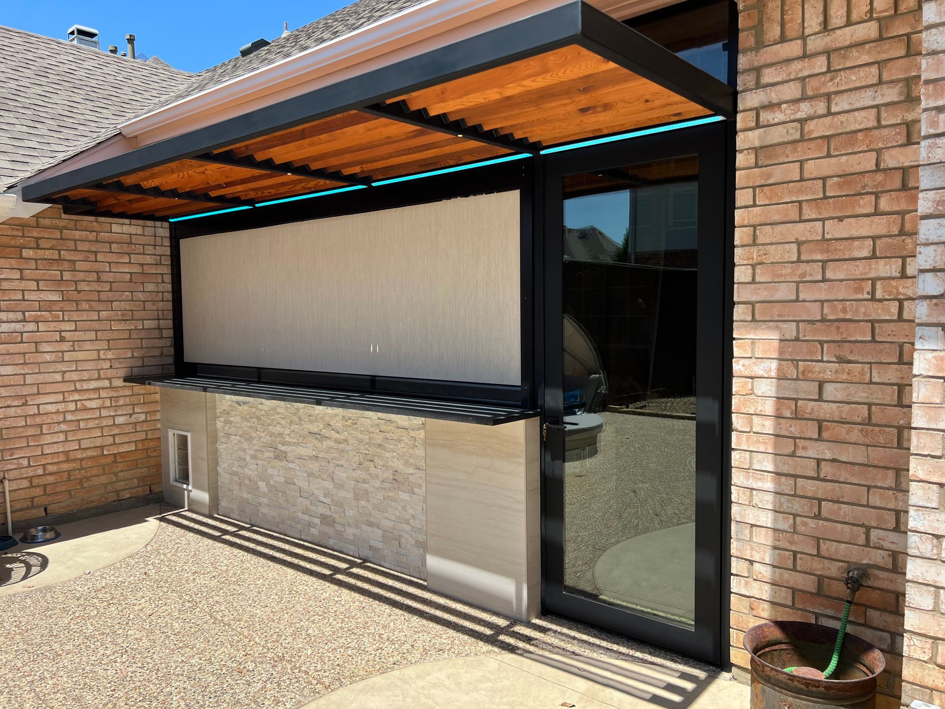 Outdoor bar area with a black and wood pergola, cream-colored wall, and brick house.