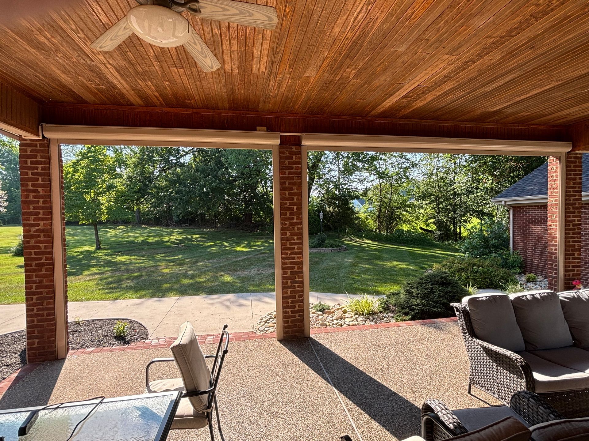 Covered patio with retractable shades, overlooking a green yard and trees.