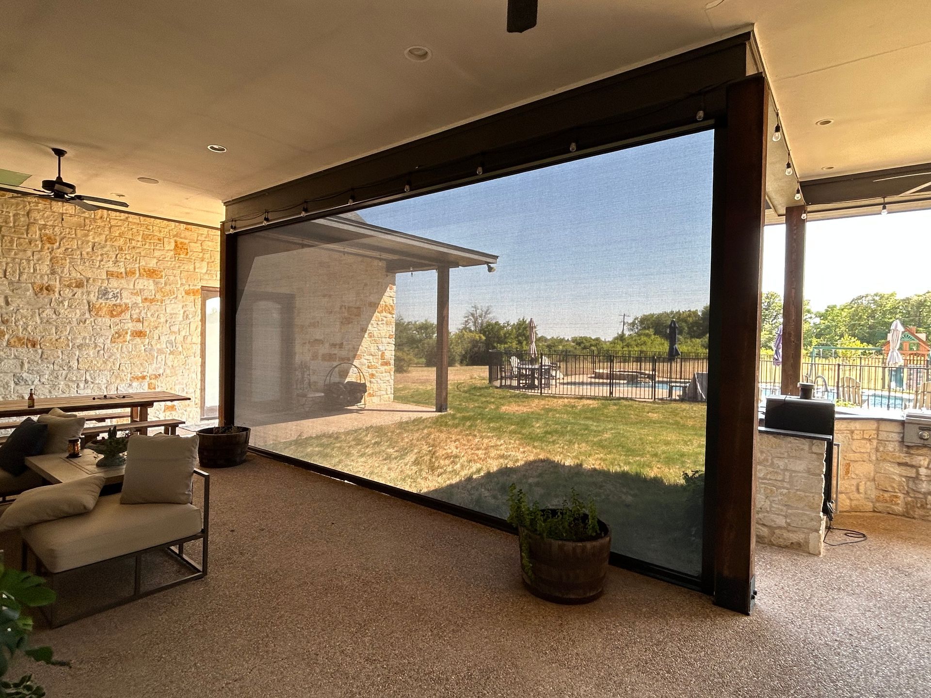 Outdoor patio with a retractable screen, stone walls, and a view of a yard and sky.