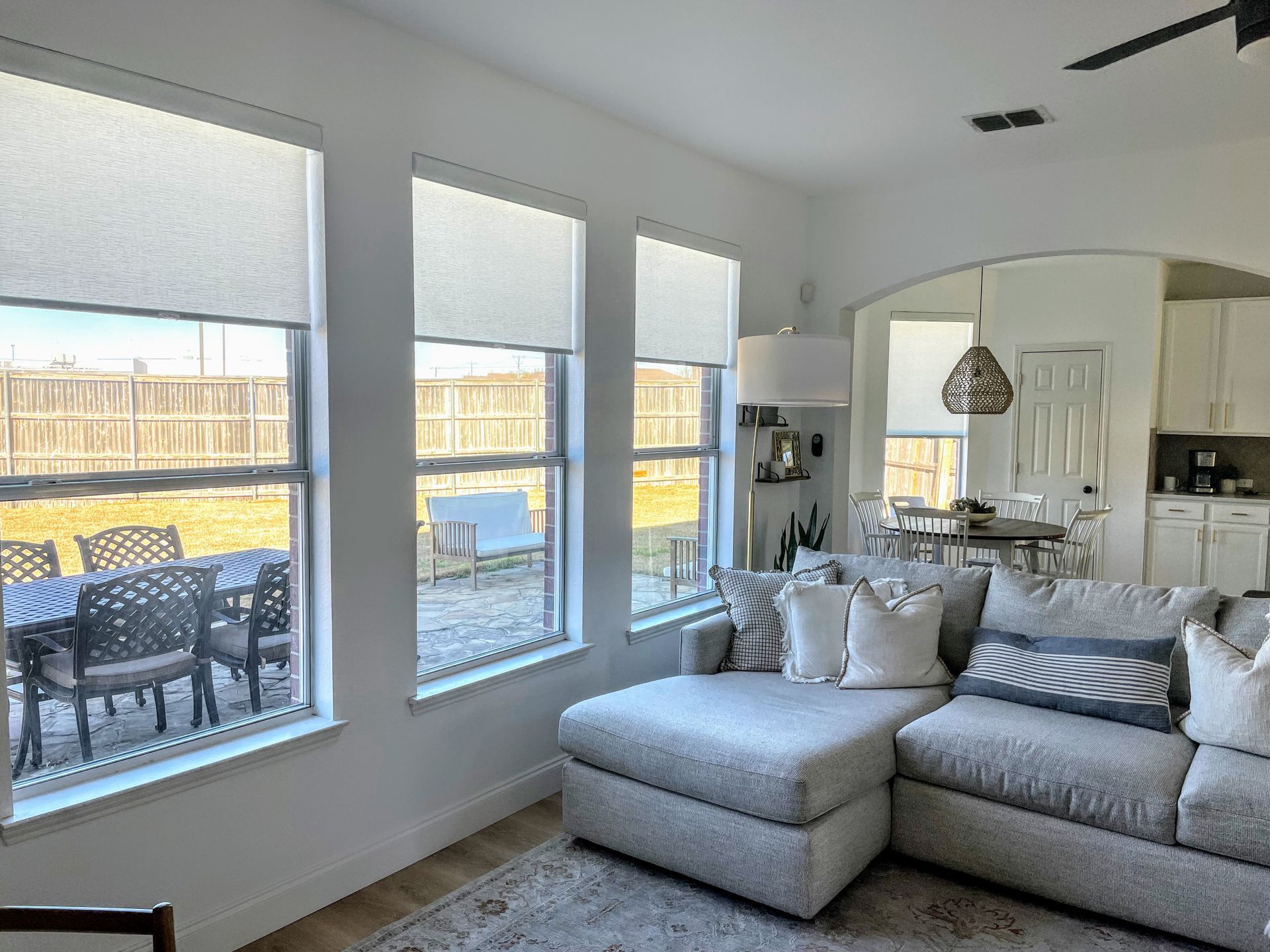 Living room with three windows, a gray sectional sofa, and a view of a backyard.