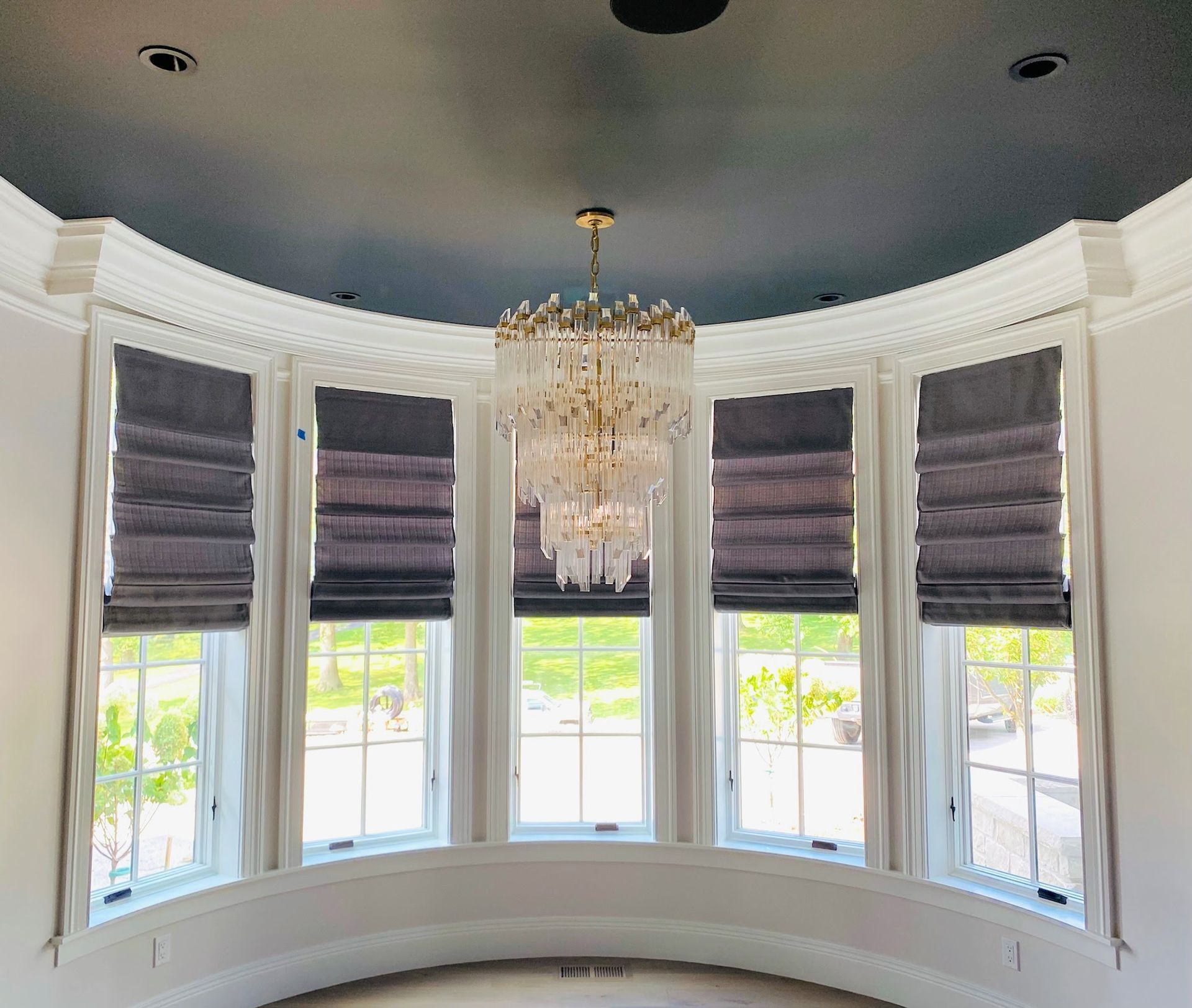 Bay window with Roman shades, a crystal chandelier, and a dark ceiling.