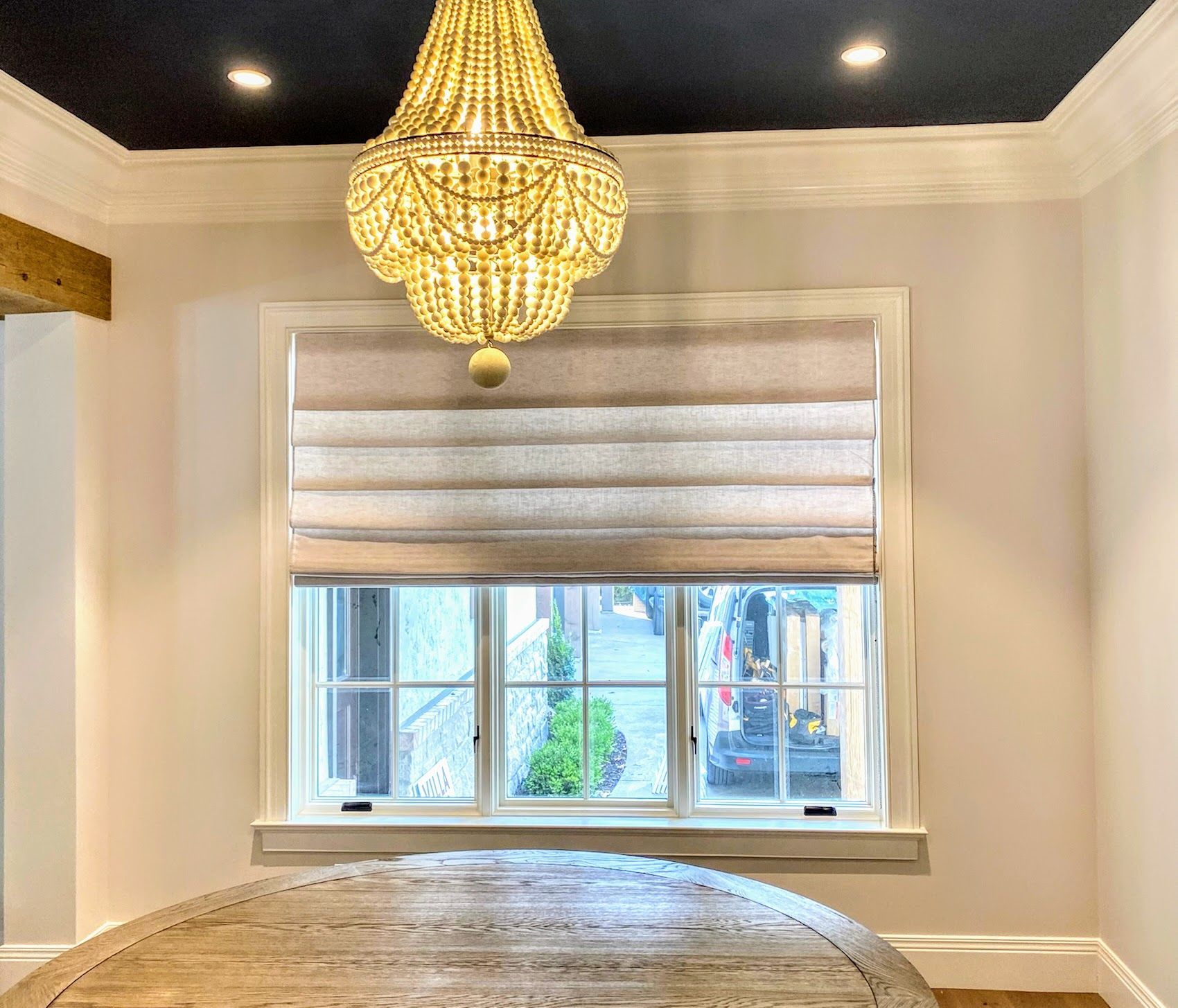 Beaded chandelier hangs above window with beige Roman shade.