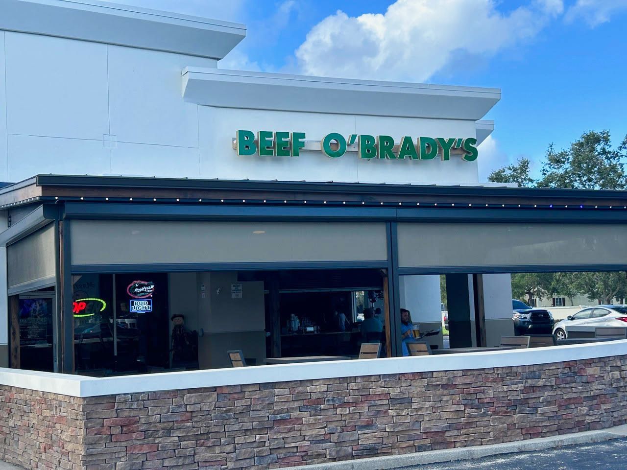 Exterior view of Beef O'Brady's restaurant with green signage, stone facade, and outdoor seating.