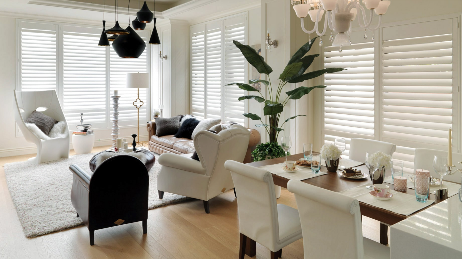 Bright, airy living room with white shutters, a dining table, and various seating areas.