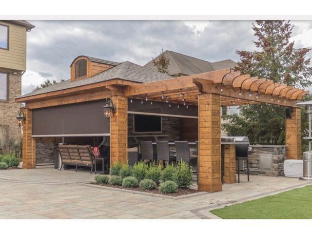 Wooden pergola with outdoor kitchen, seating, and a retractable shade.