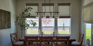 Dining room with wooden table and chairs, large windows with shades, and a chandelier.