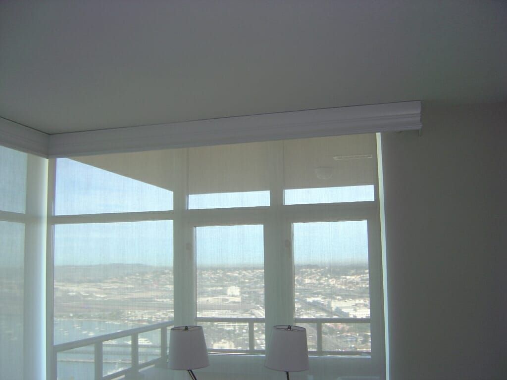 Interior corner with large windows, sheer roller shades, city view.