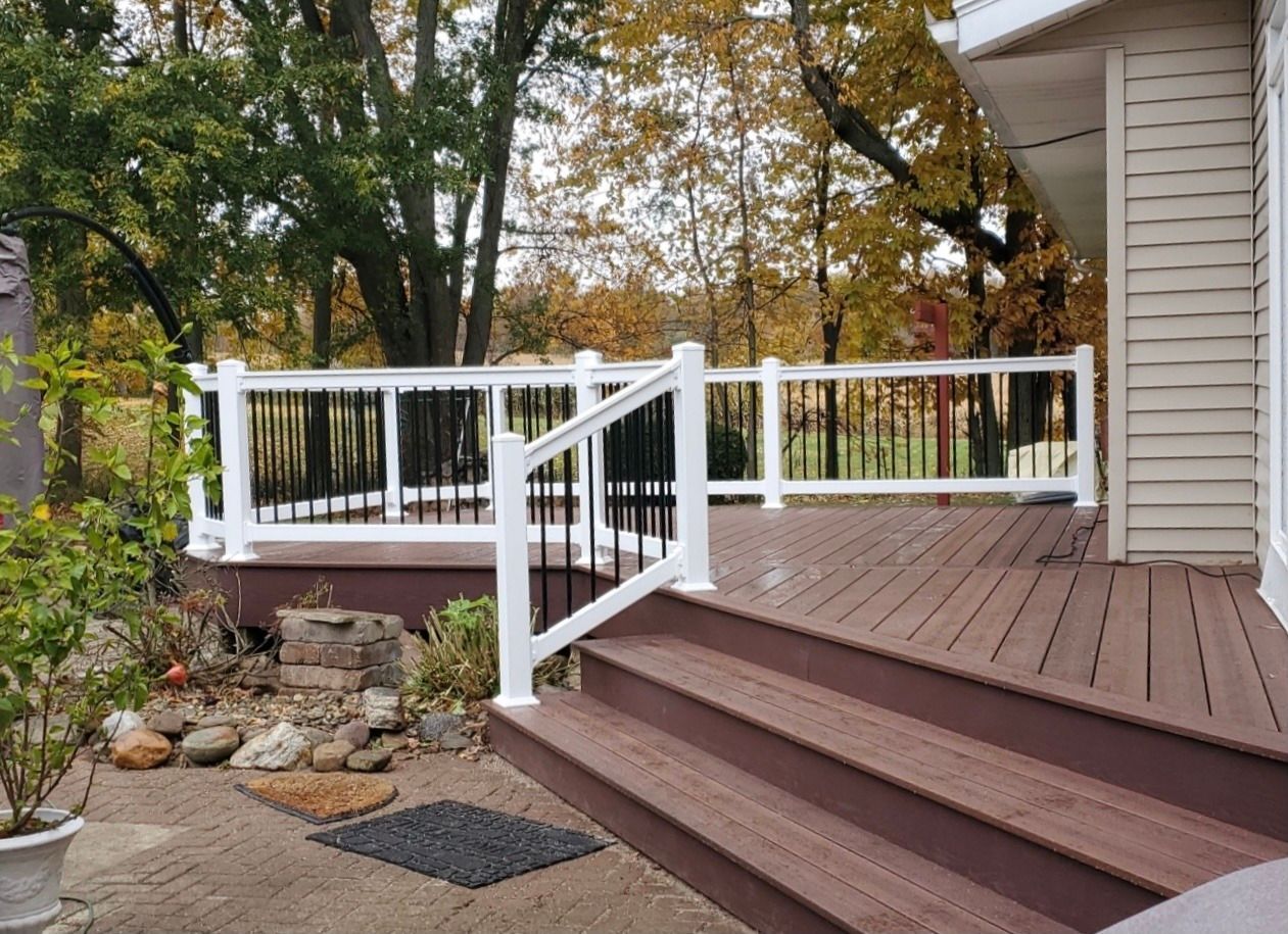 Deck with composite wood, white railing, black vertical bars, and steps leading to a patio.