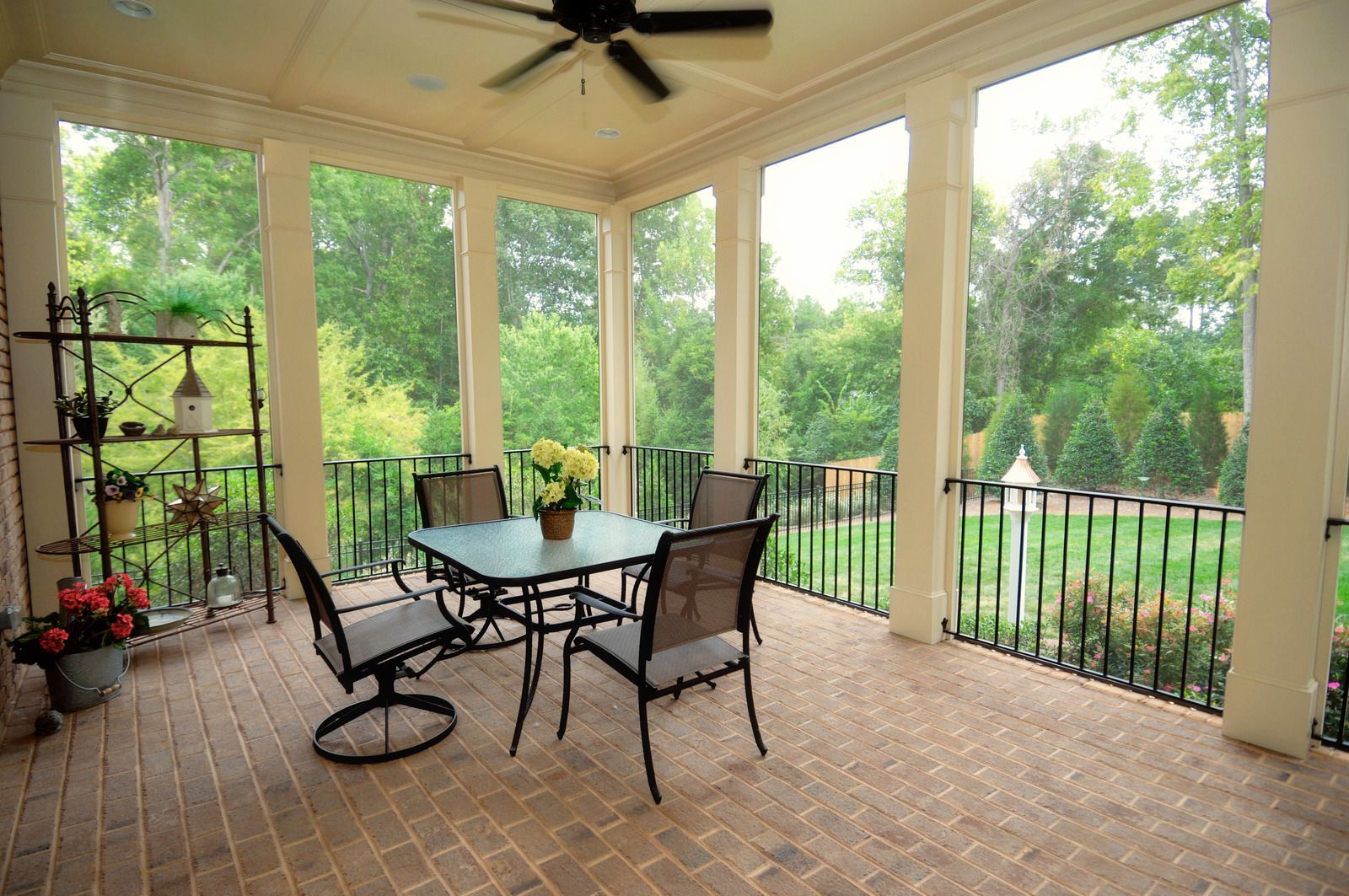 A screened in porch with a table and chairs and a ceiling fan.