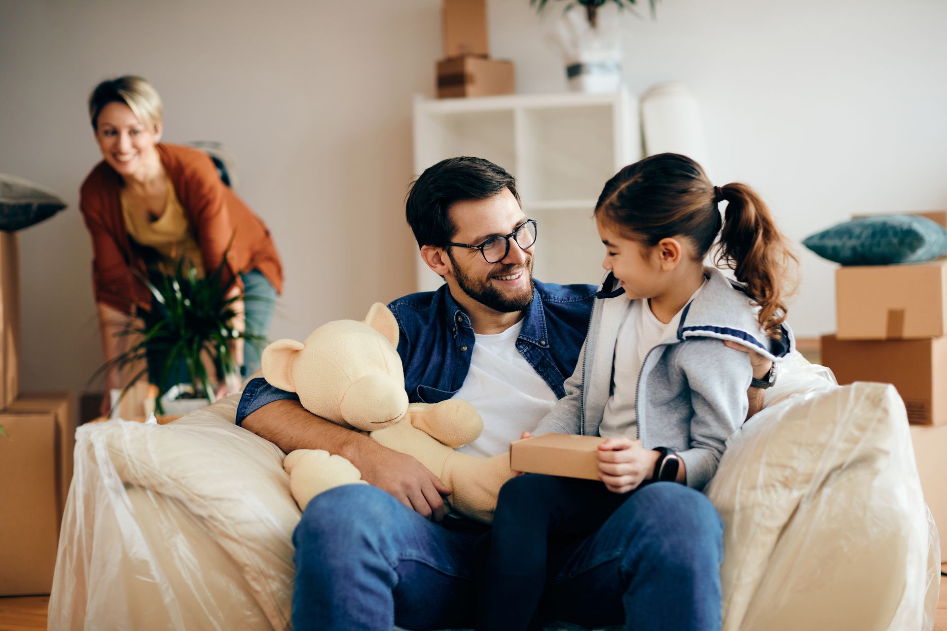 Family sitting on a couch with a child, chatting in a cozy living room; another adult stands nearby.