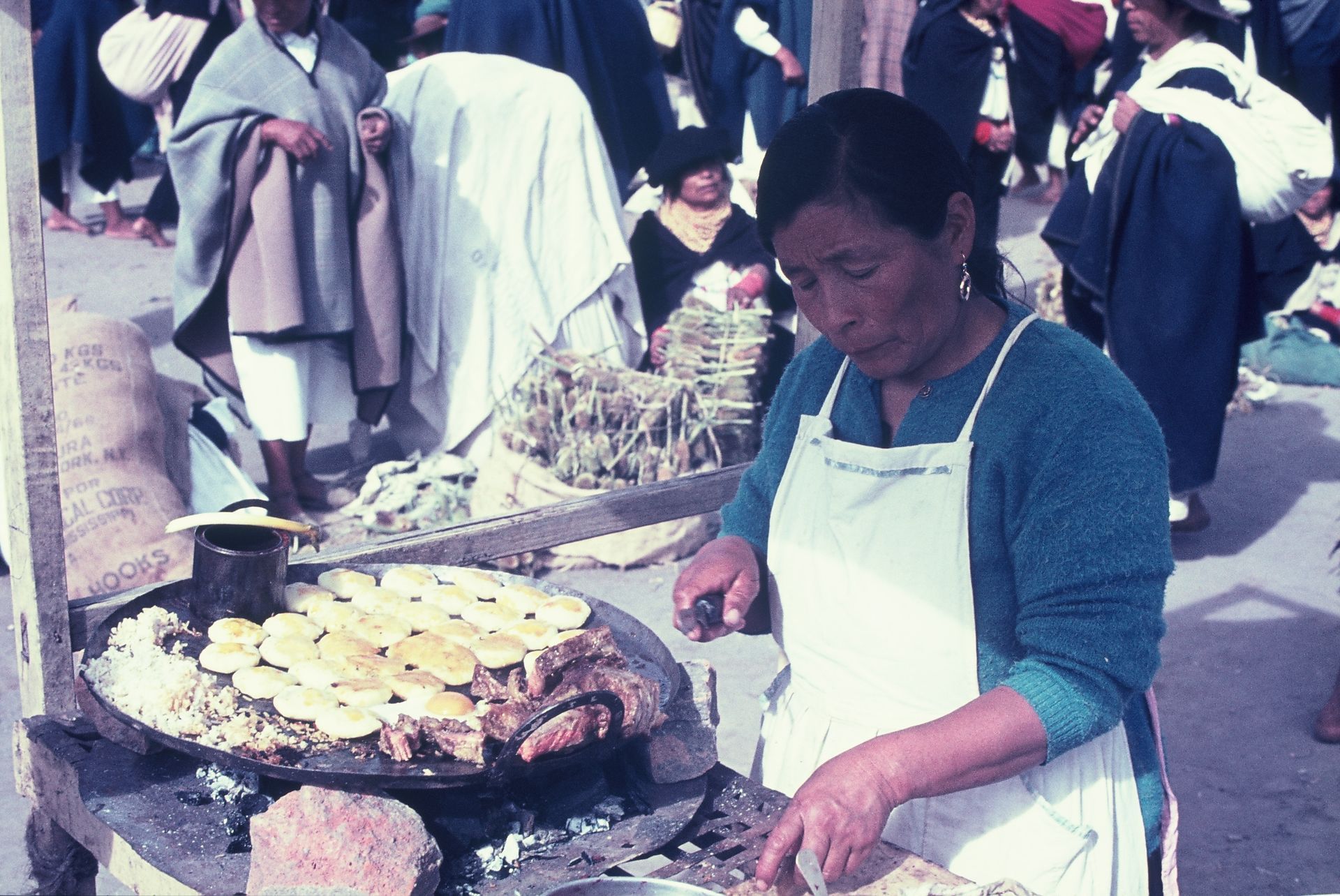 A woman in an apron is cooking food in front of a crowd