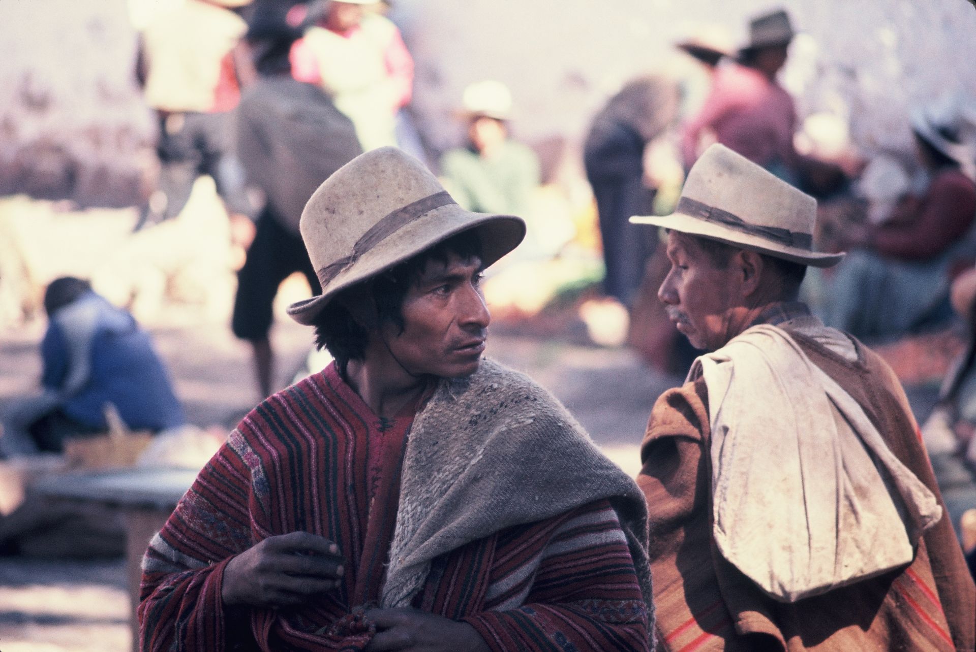 Two men wearing hats are talking to each other in a crowded area.