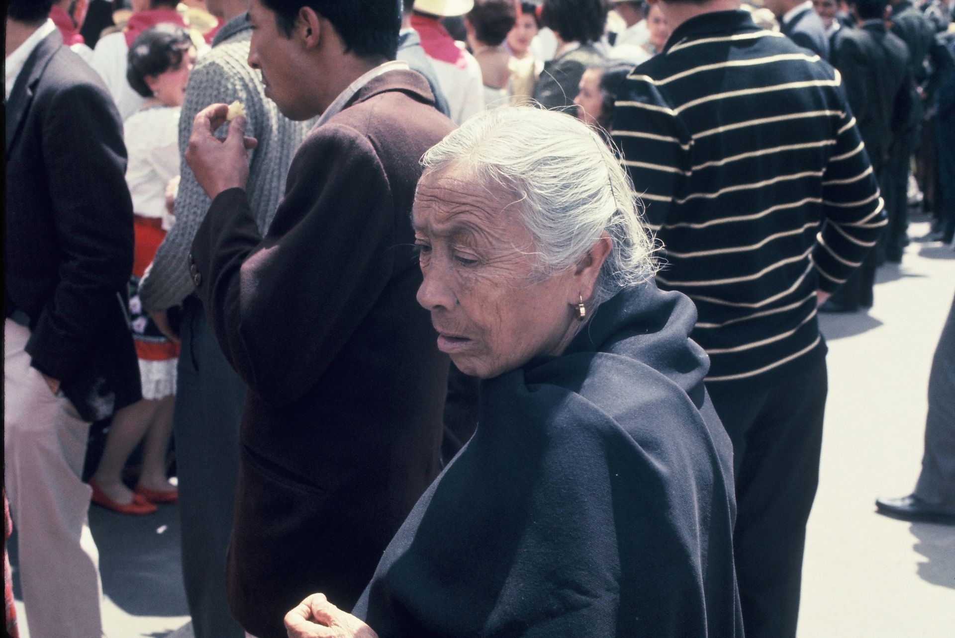 A woman in a black cape is standing in a crowd of people.