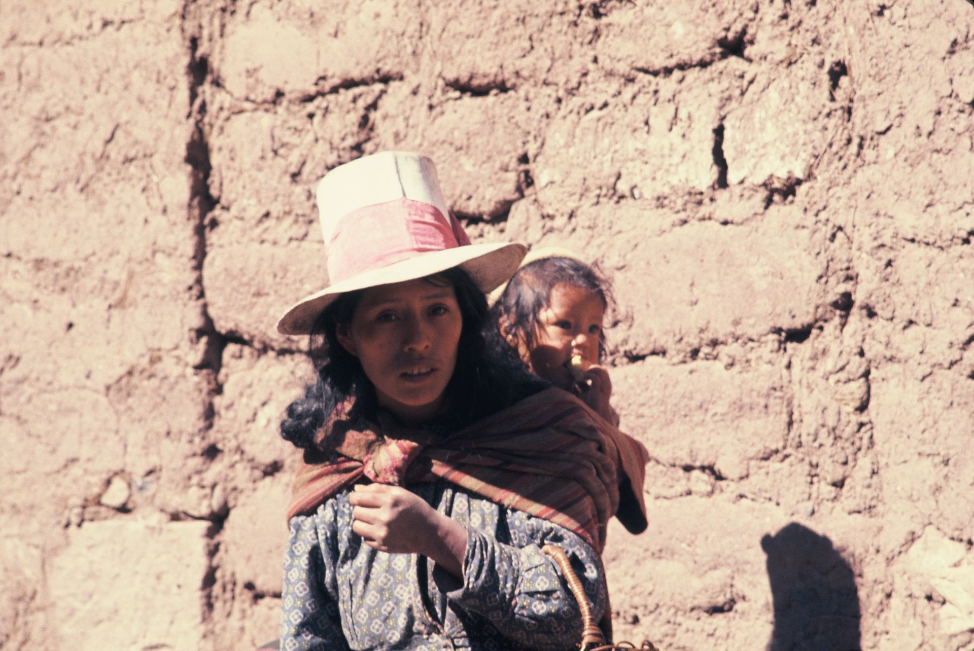 A woman wearing a hat is carrying a baby on her back