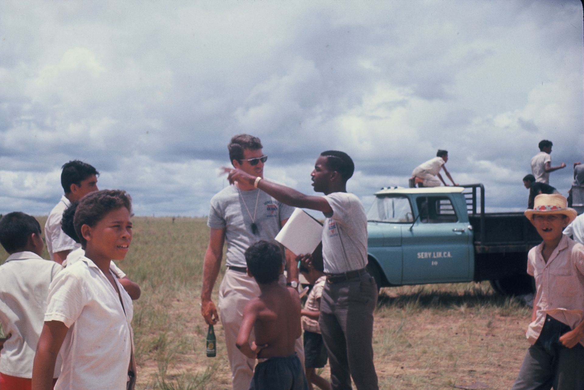 A group of people are standing in a field with a truck in the background.