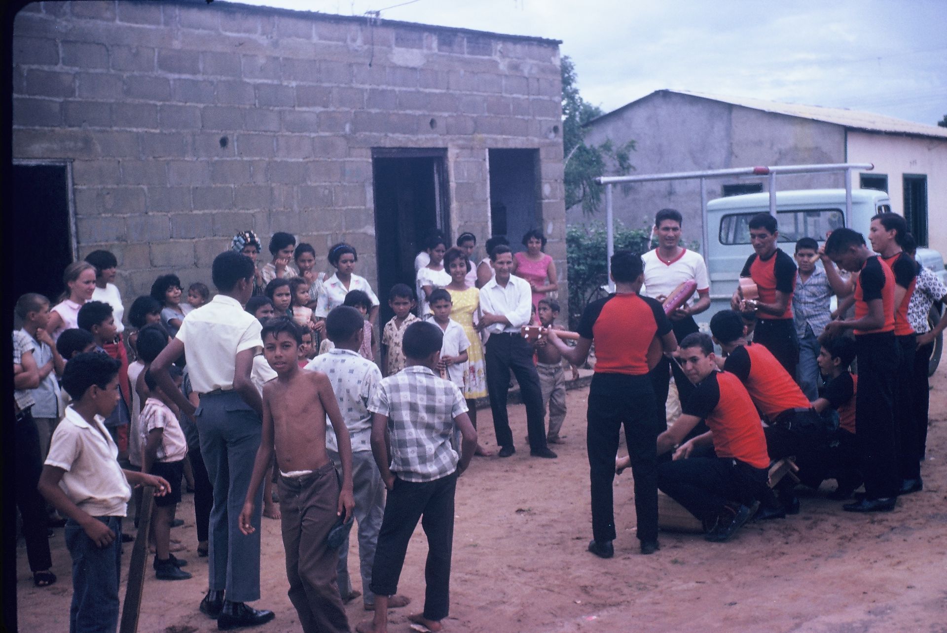 A group of people are gathered in front of a building with a white van in the background