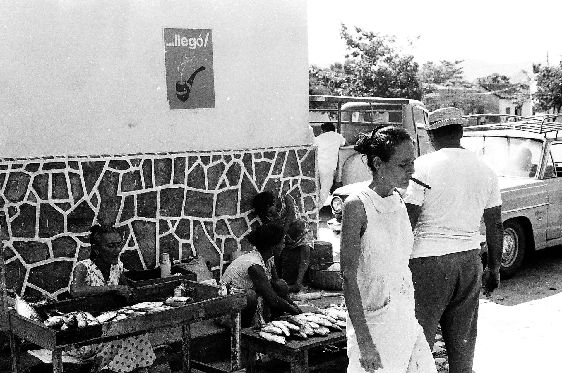 A black and white photo of people at a market with a sign that says