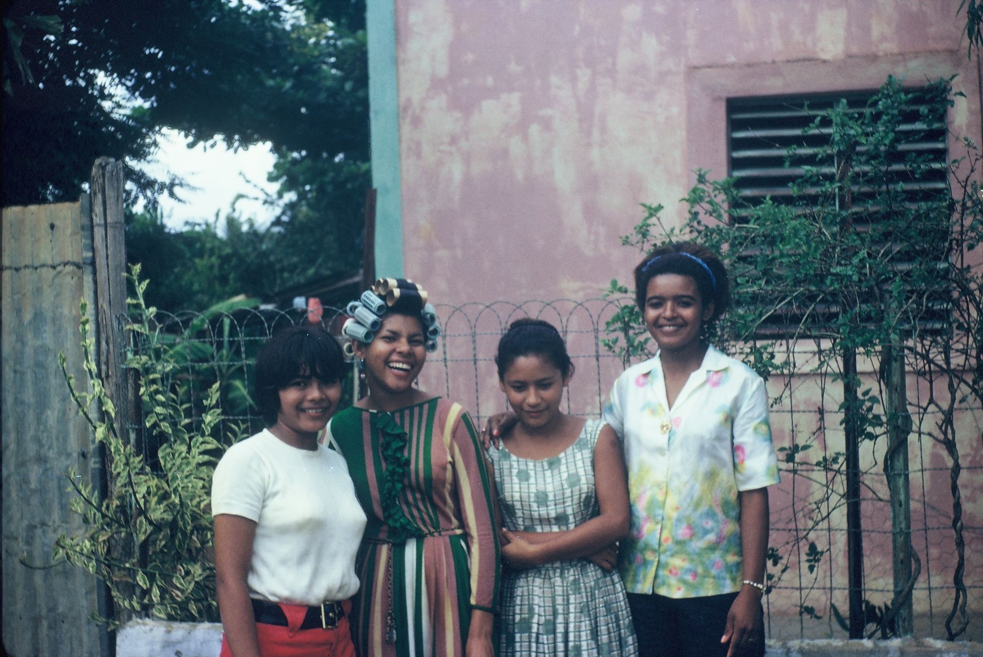 Four women are posing for a picture in front of a pink building.