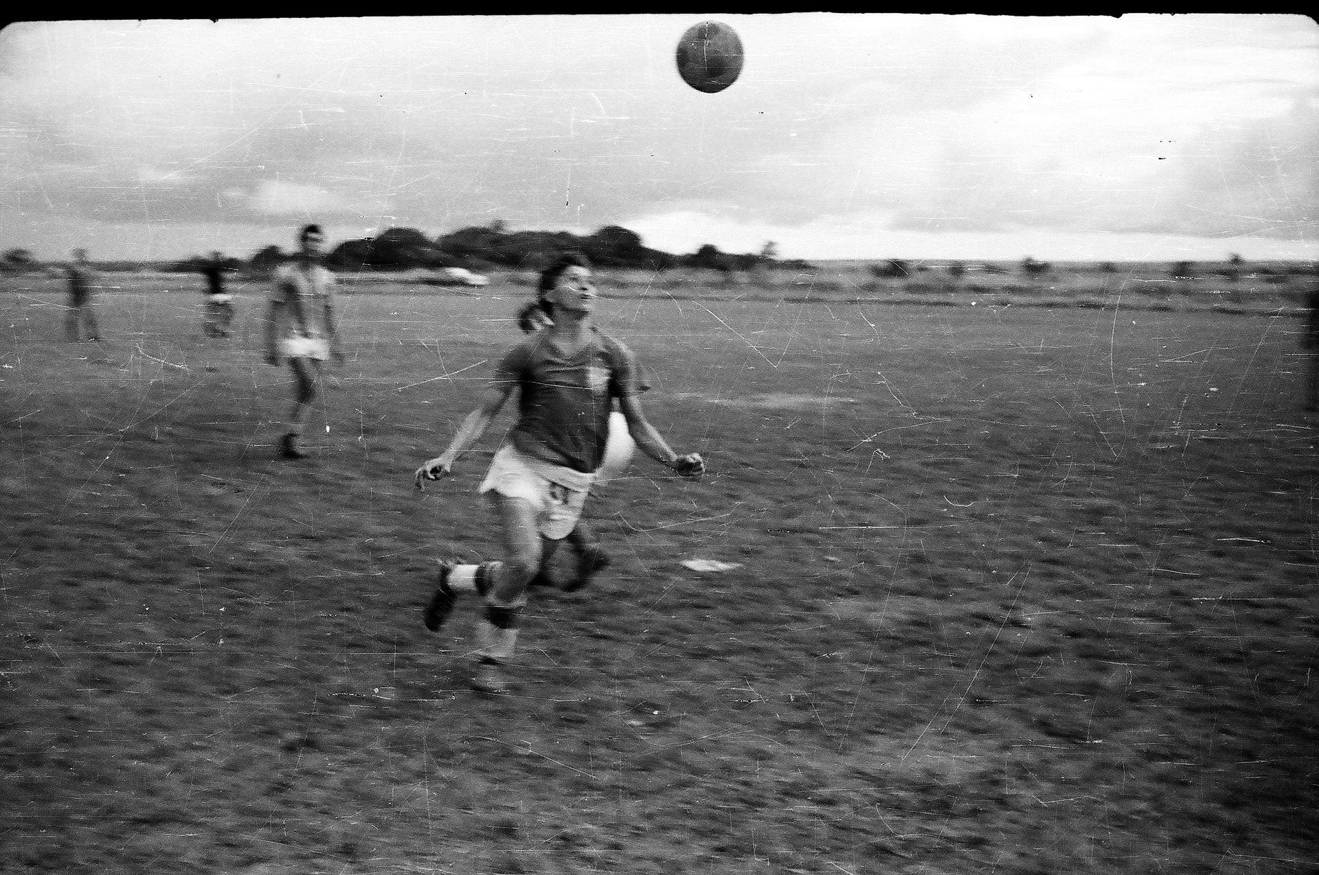 A black and white photo of a group of people playing soccer on a field.