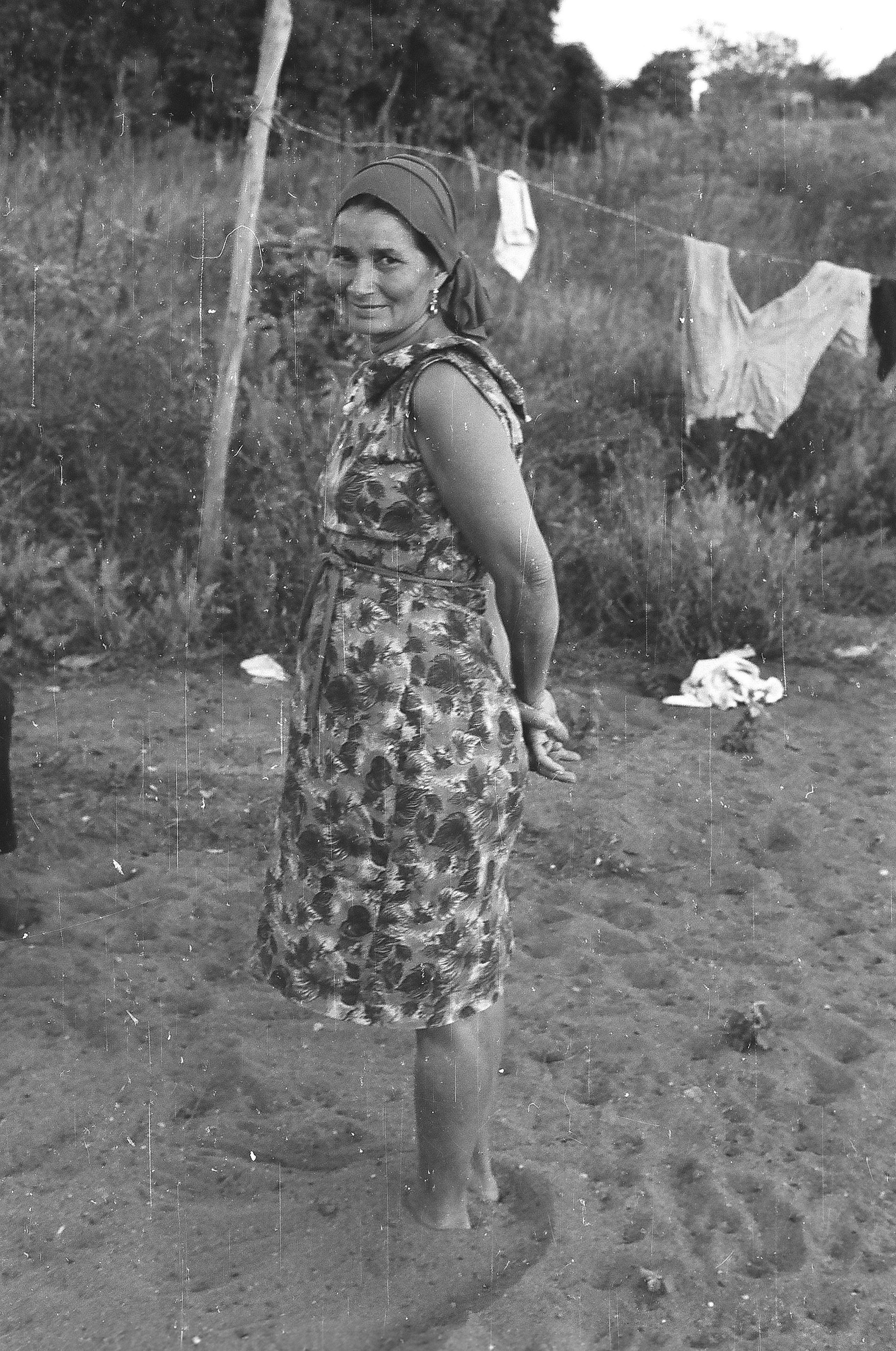 A black and white photo of a woman in a dress standing in the dirt.