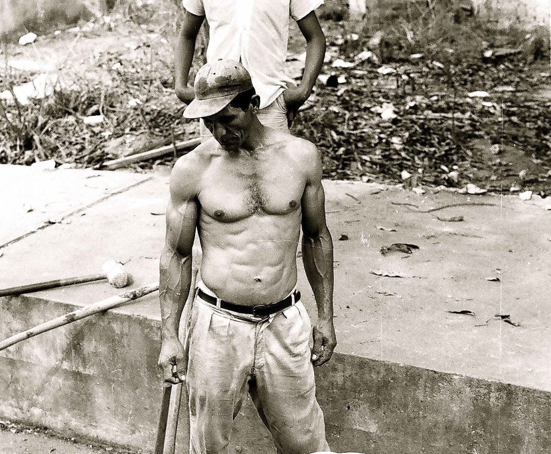 A black and white photo of a shirtless man holding a baseball bat