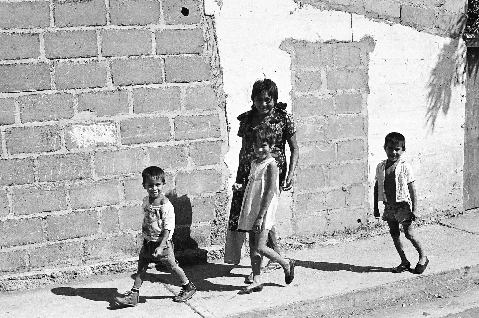 A black and white photo of a woman and two children walking down a sidewalk