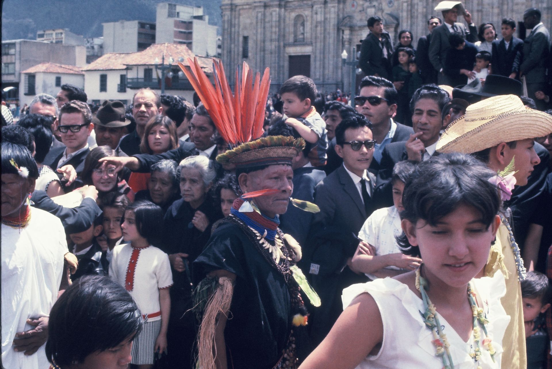 A crowd of people are gathered around a man wearing a feathered hat