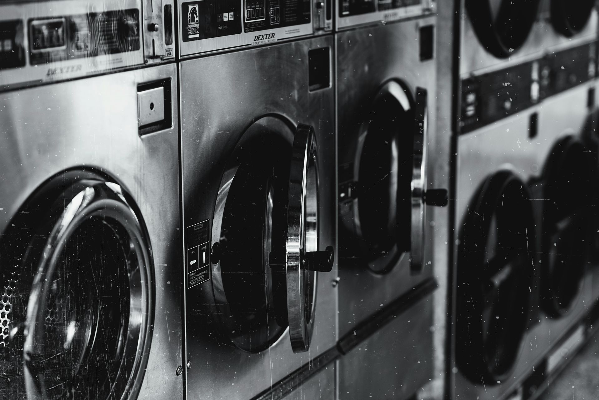 A black and white photo of a row of washing machines in a laundromat.