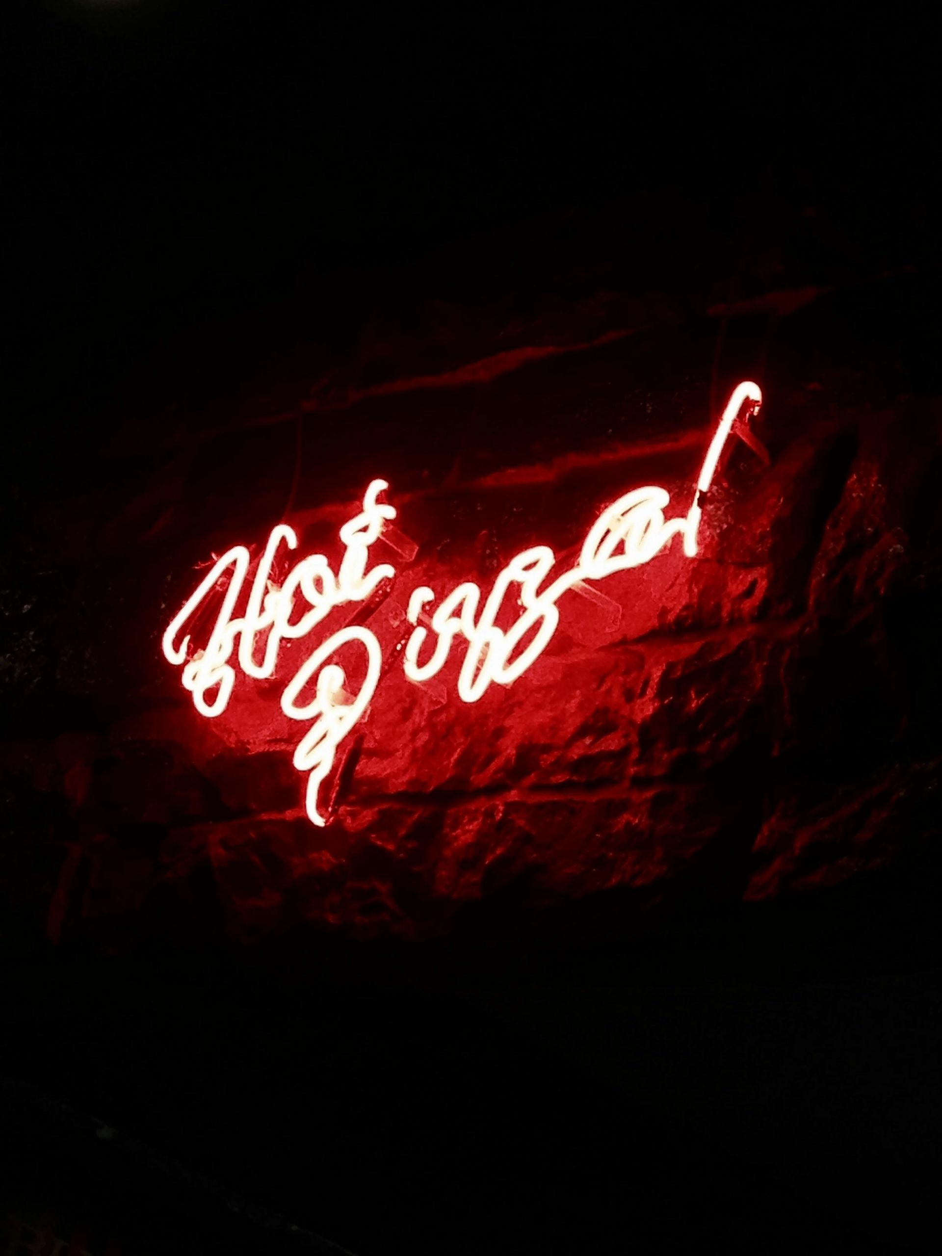 A red neon sign that says `` hot pizza '' on a black background.