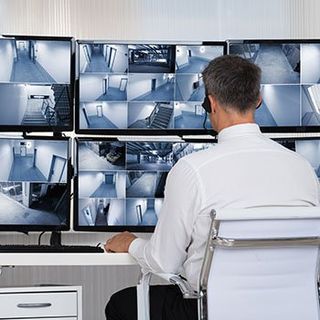 A man is sitting at a desk looking at a bunch of monitors.