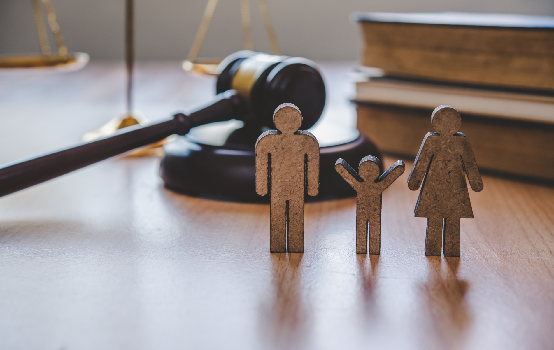 Wooden family figures near a gavel, books, and balance scale on a wooden table.