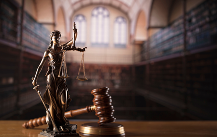 Statue of Lady Justice with scales and gavel in a library, symbolizing law and justice.