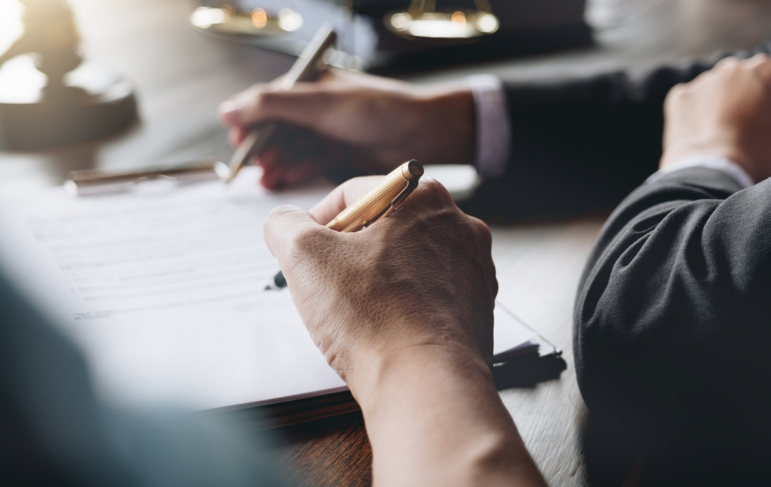 Hands signing legal documents at a desk; courtroom setting with a gavel in the background.