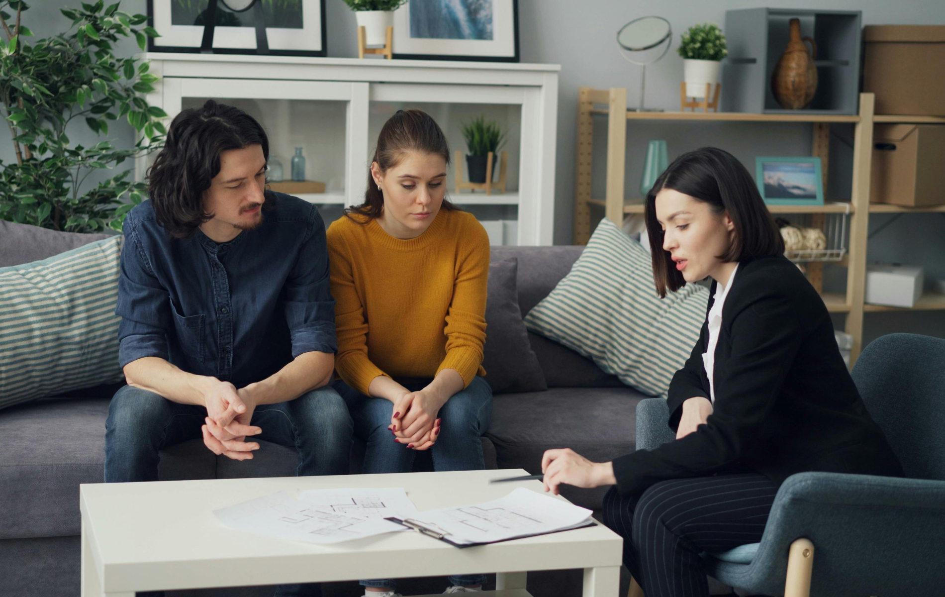 A professional sits in an armchair, discussing documents on a coffee table with two people seated on a sofa nearby.