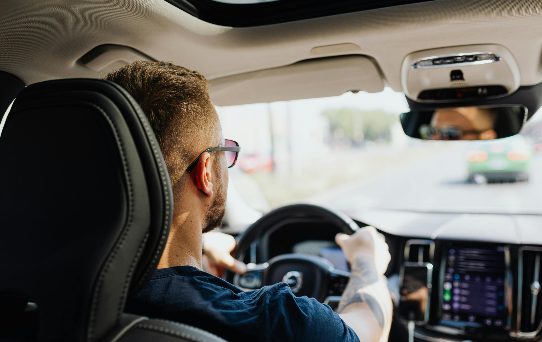 Man driving a car, hands on the steering wheel, looking forward.