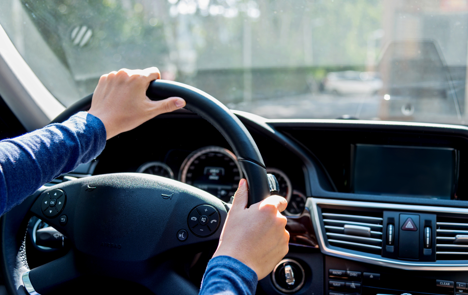 Hands on a car steering wheel, driving in daylight.