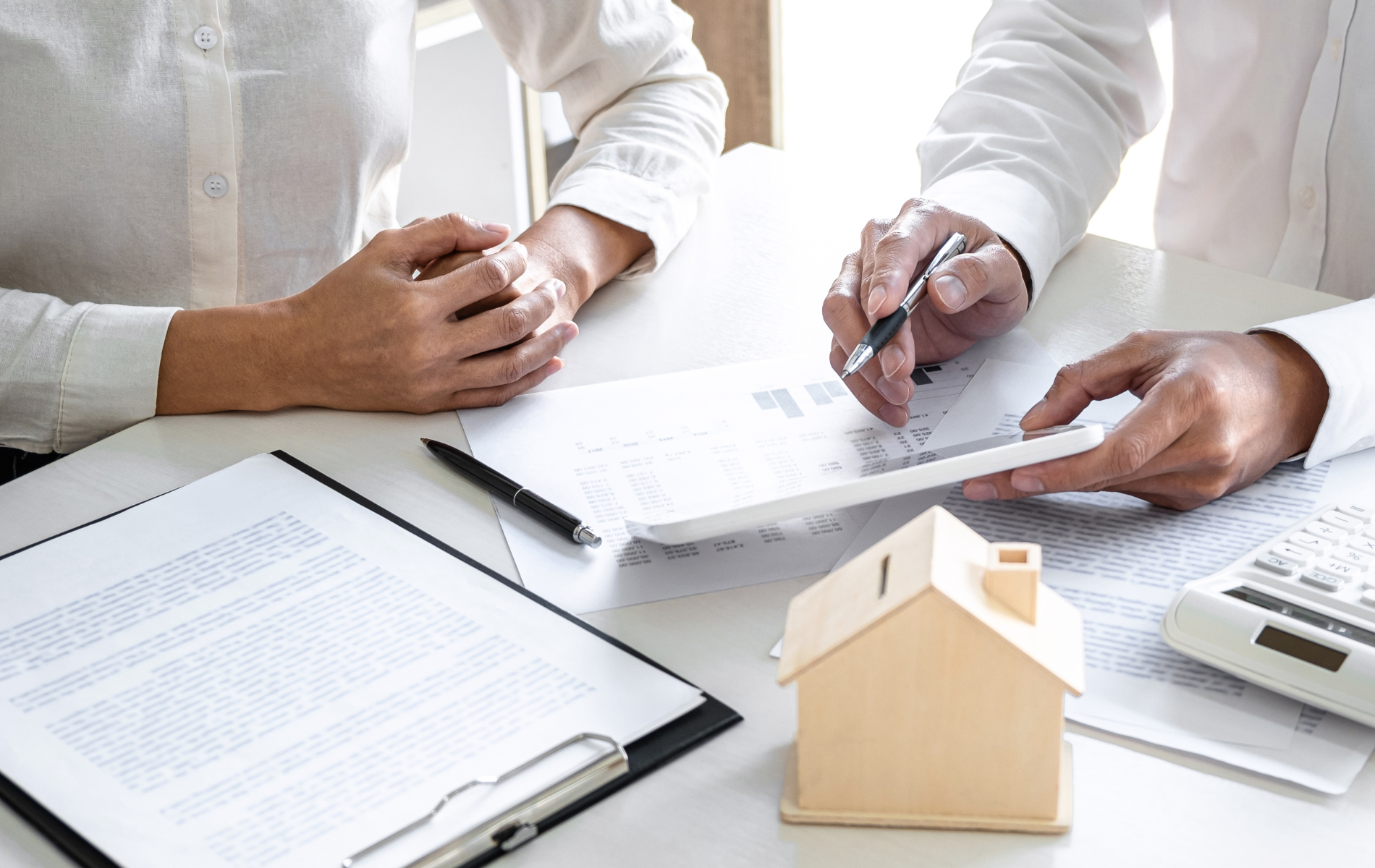 Two people reviewing documents and using a calculator at a table with a model house.