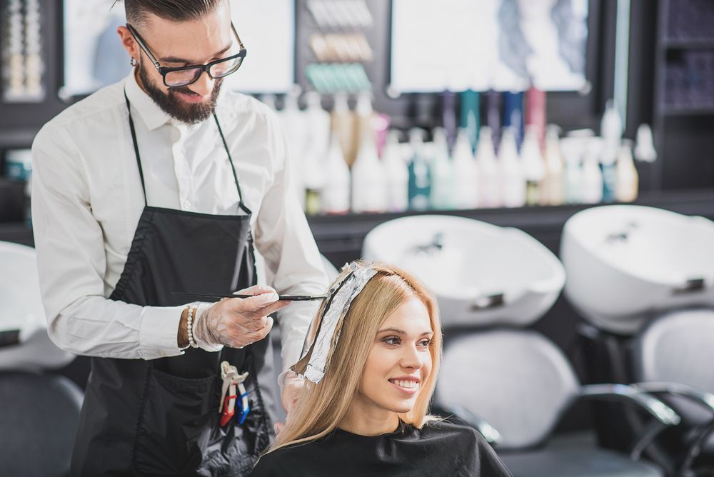 A stylist applies hair dye to a customer's blonde hair in a salon setting.