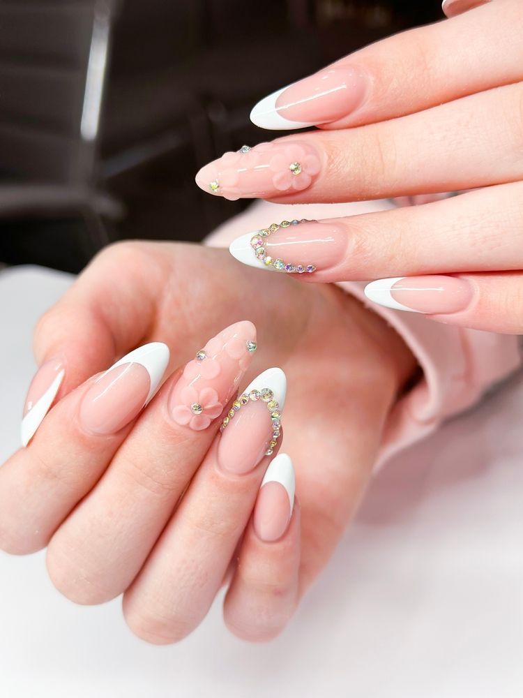 Close-up of hands with French tip acrylic nails, accented with gems and floral details.