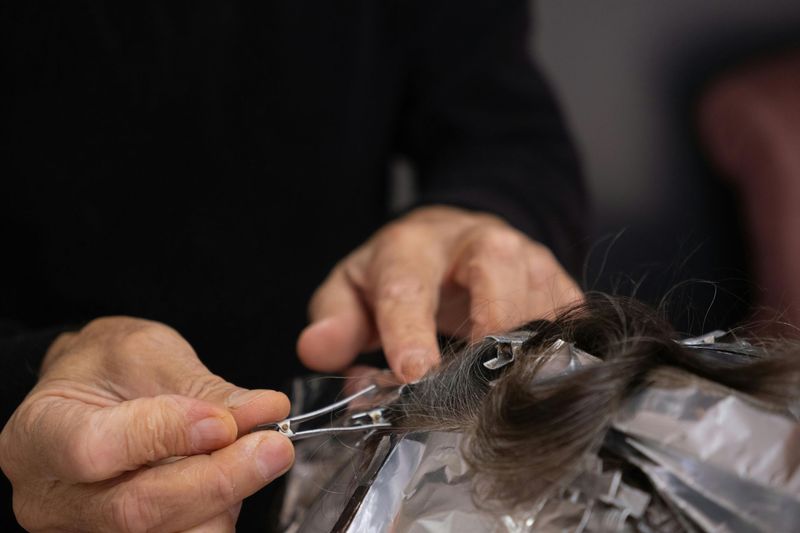 Hands using scissors to cut hair over a foil-covered section.