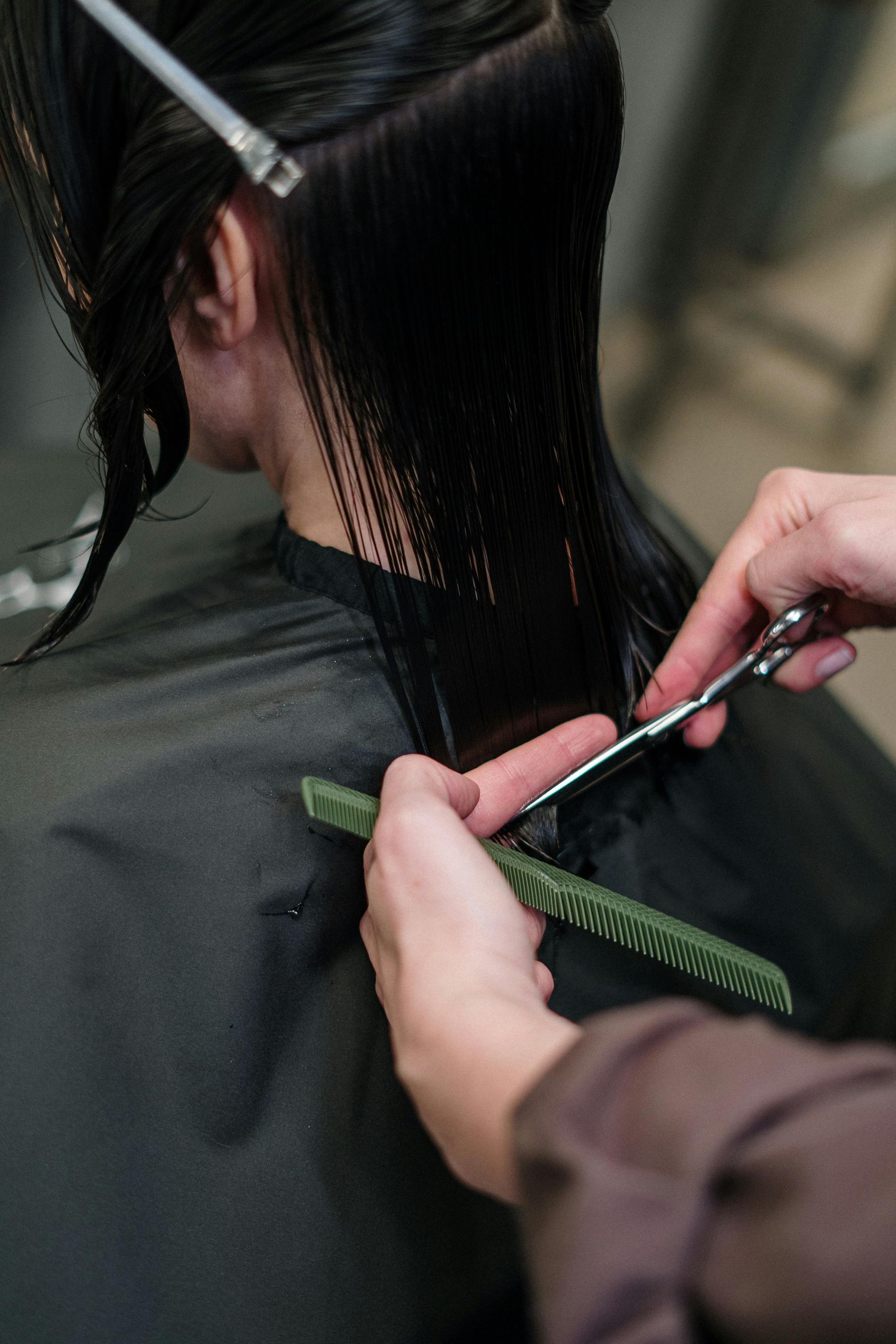 Hairdresser cutting wet, dark hair with scissors and comb.